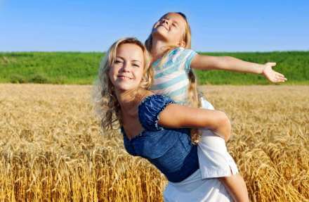 Mom in wheat field giving piggy back ride to daughter