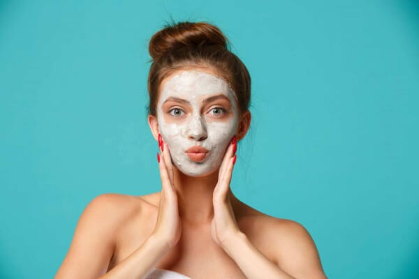 Beauty treatment - woman applying clay face mask