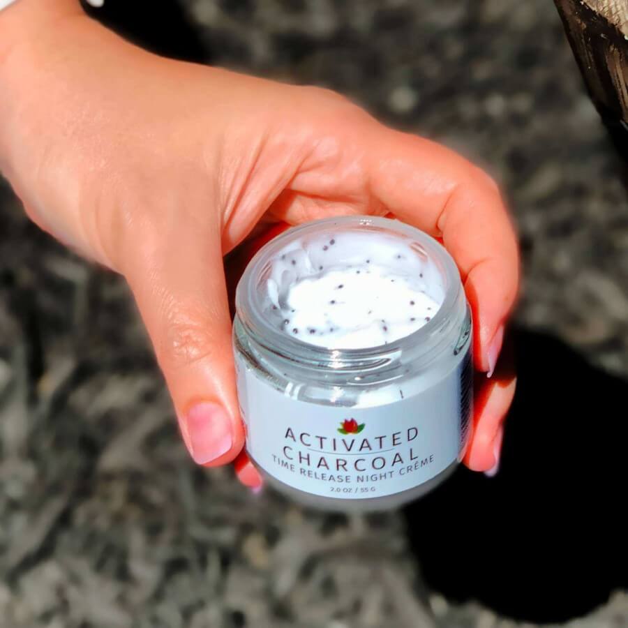 female hand holding open jar of activated charcoal night creme