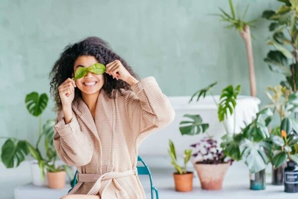 female in bathrobe holding two plant leaves in front of her eyes