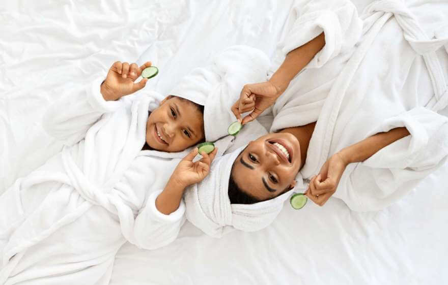 mother and daughter on bed in robes with cucumbers for spa treatment