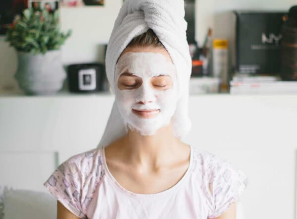 female with towel on head sitting with facial mask