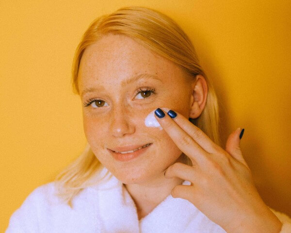 female applying moisturizer on yellow background