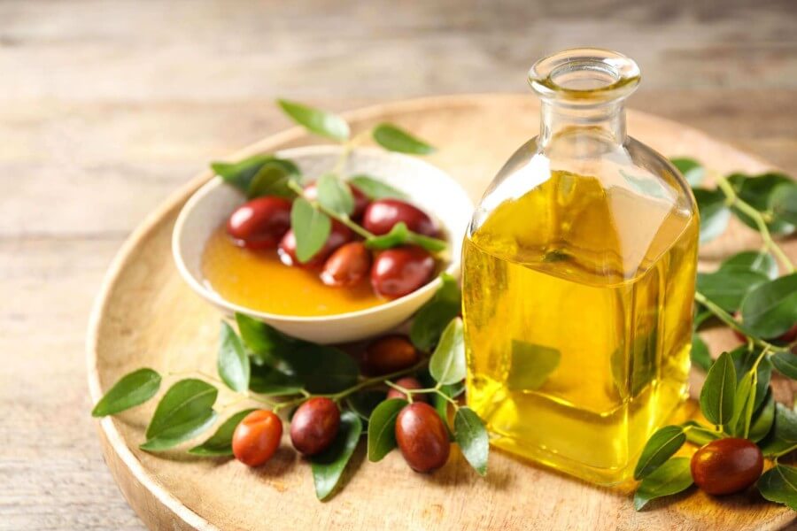 Glass bottle with jojoba oil and seeds on wooden table