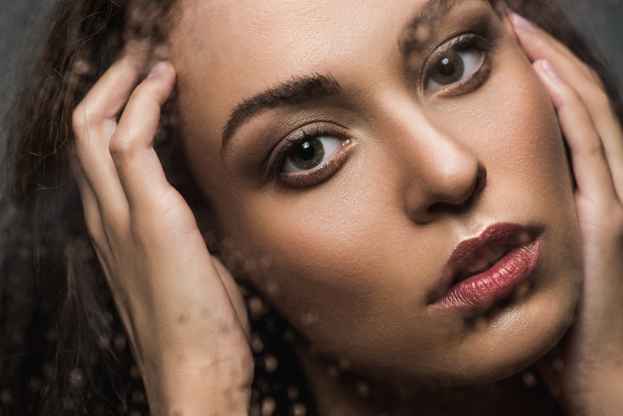 beautiful tender woman behind wet glass looking at camera