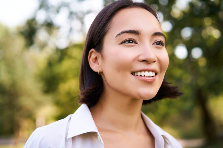 close up face of asian happy girl, smiling and looking at camera carefree, walking in park