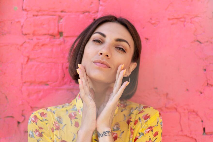 stylish woman in yellow summer dress on background of pink brick wall happy calm and positive