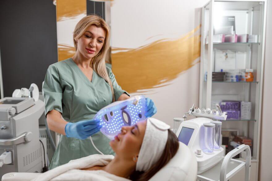 expert beautician making cosmetic procedure with led facial mask. photon therapy