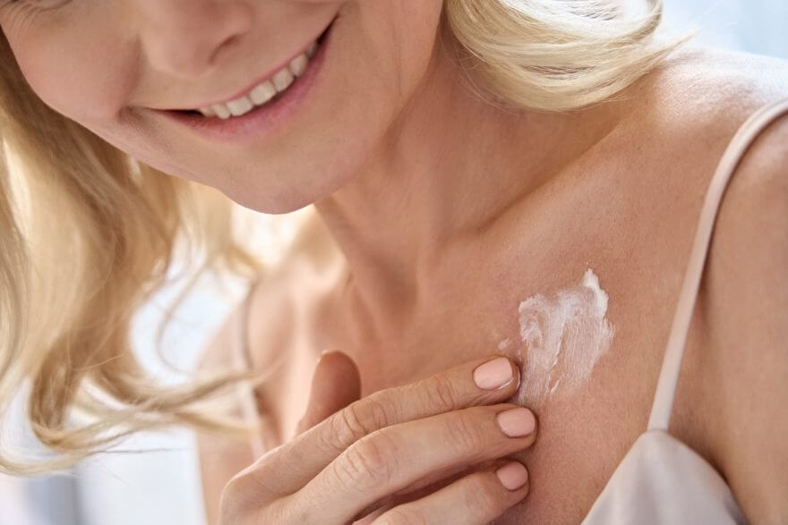 happy middle aged woman applying cream moisturizing lotion on body skin.