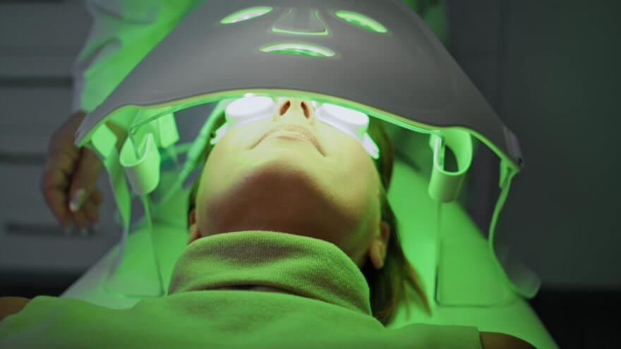 woman lying phototherapy clinic close up. beautician checking led light mask.