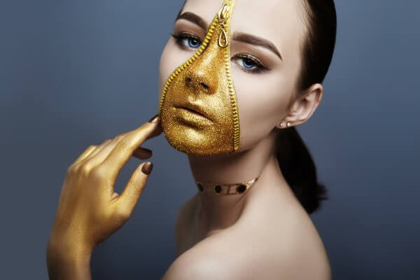 creative grim makeup face of girl golden color zipper clothing on skin. fashion beauty creative cosmetics and skin care halloween. brunette woman on dark background, beautiful big eyes and smooth skin