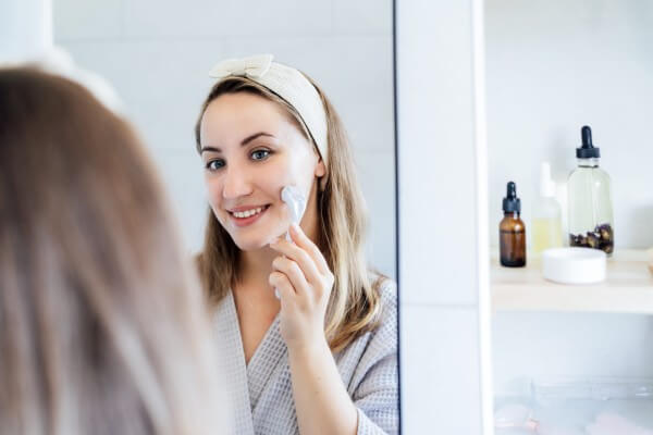 young woman in bathrobe looking in mirror and making face massage with micro needle meso derma roller. concept of natural procedures for skin care. home beauty self care treatment. selective focus.