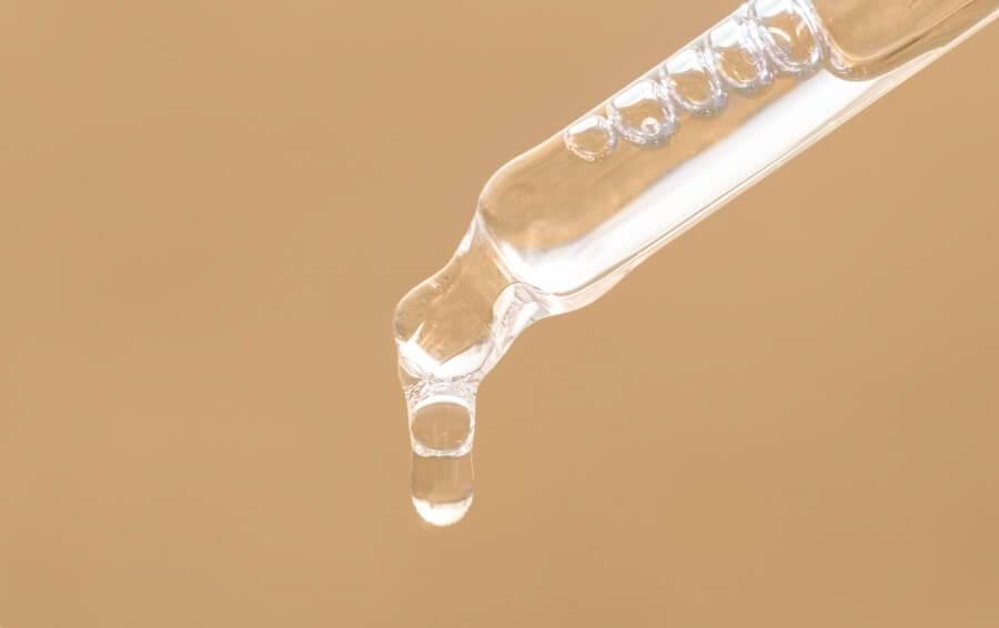 pipette with essential oil, serum with peptides, emulsion, hyaluronic acid on beige background. closeup of beige dropper, falling drop of oil close up. beauty skincare product.