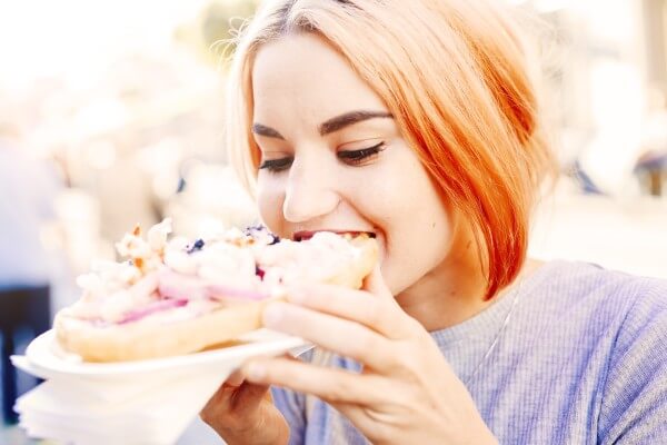 young woman eating pie outdoors.