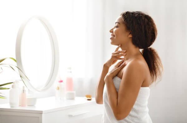 beautiful black lady touching soft skin on neck and looking in mirror