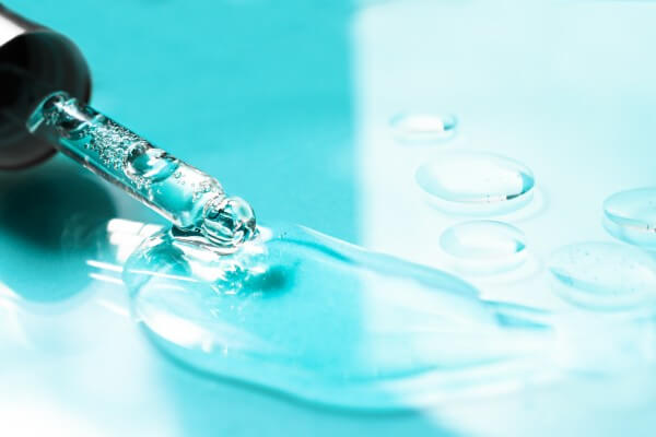 hyaluronic acid flowing out of a glass pipette on a colored background. transparent cosmetic product close up.