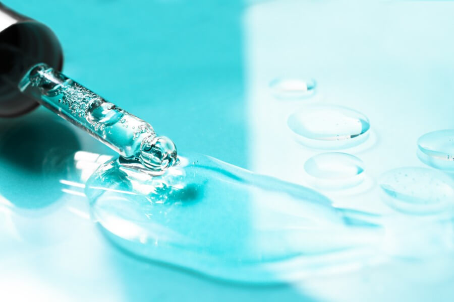 hyaluronic acid flowing out of a glass pipette on a colored background. transparent cosmetic product close up.