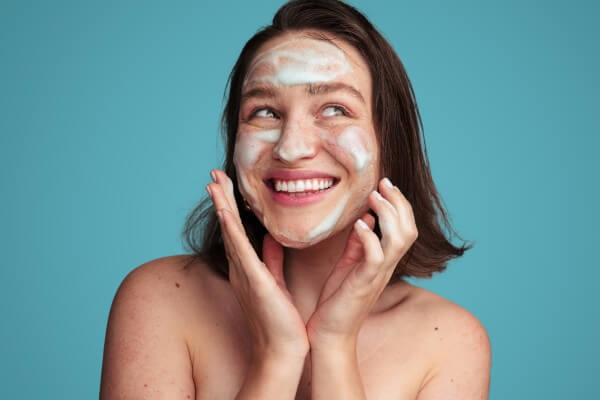 joyful female millennial washing face with foam cleanser during beauty routine