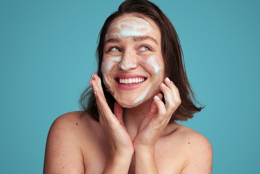 joyful female millennial washing face with foam cleanser during beauty routine