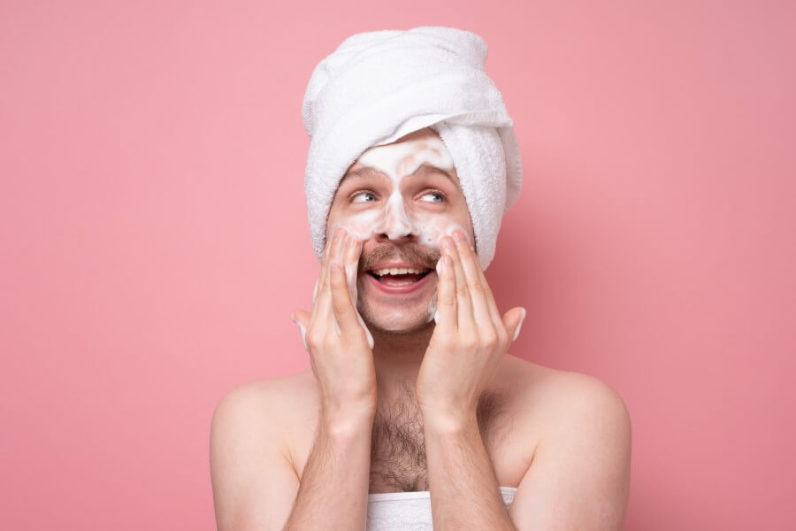 surprised man washes face with cleanser and soap, has foam on skin