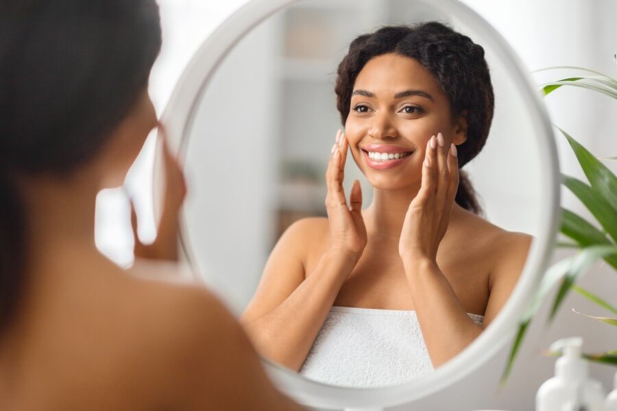 beauty concept. attractive young black woman looking at mirror in bathroom