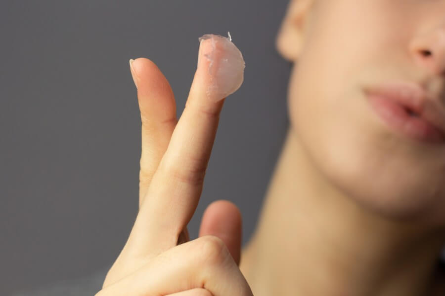 a young woman is applying petroleum jelly to her face. concept of slugging.