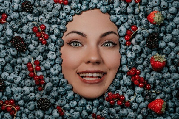 excited woman face in fresh ripe berries blueberries, organic bilberry plant