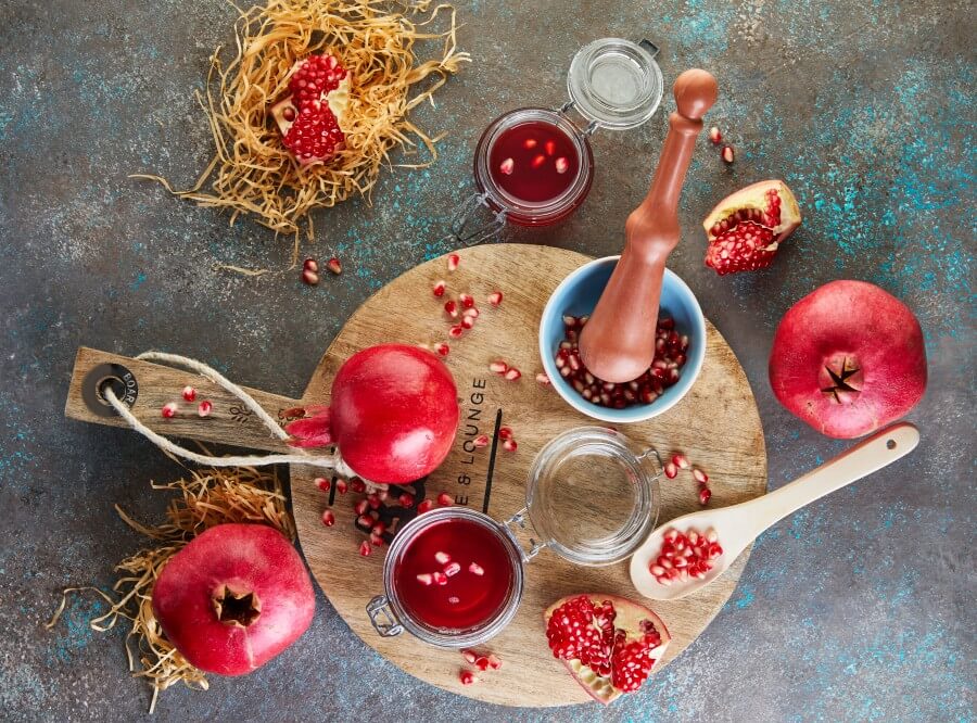 homemade sweet red pomegranate syrup in jars with pomegranate seeds on a wooden stand