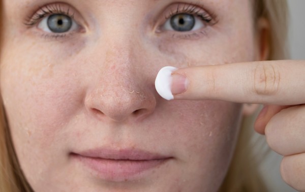 a woman examines dry skin on her face. peeling, coarsening, disc