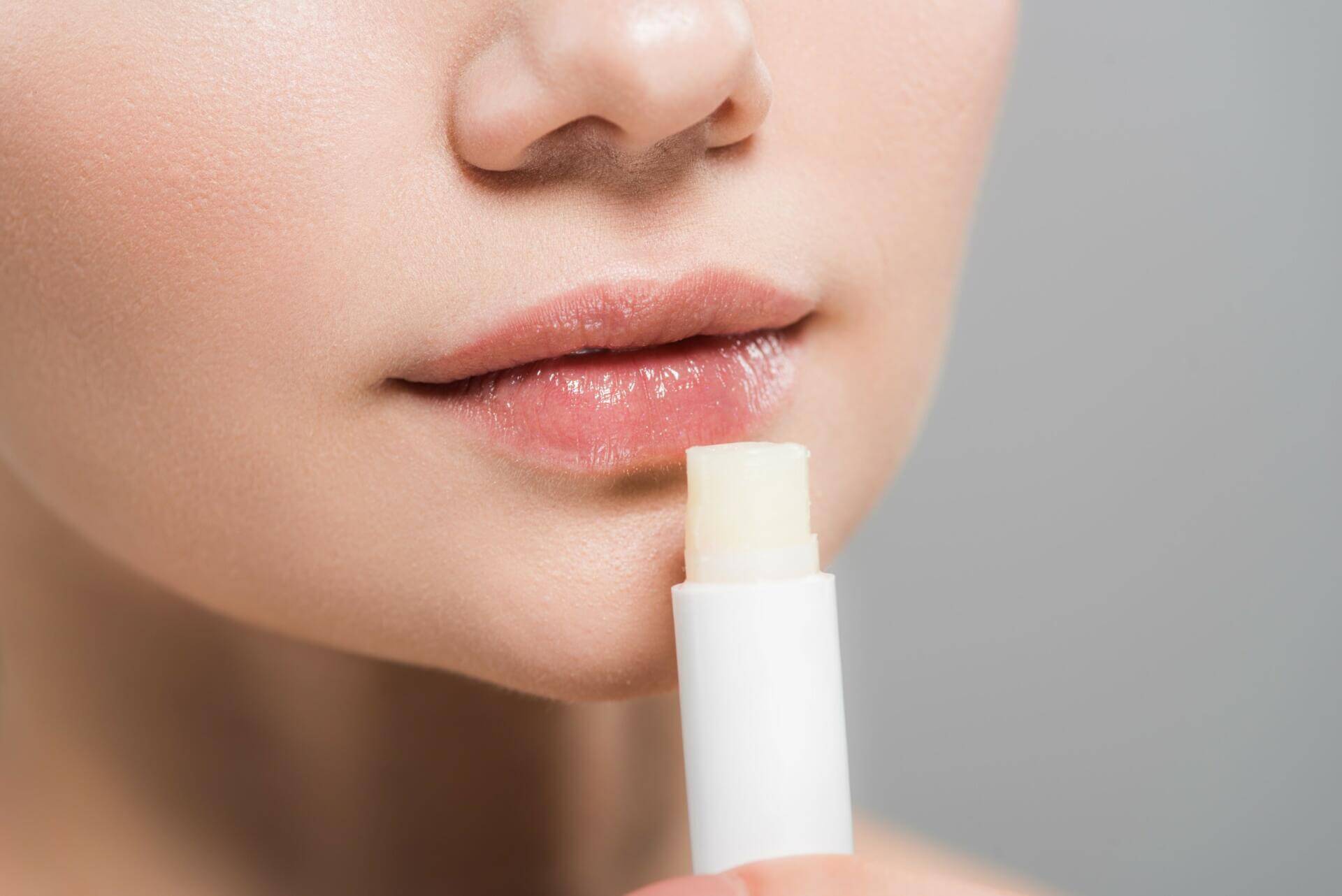 cropped view of young woman holding lip balm isolated on grey