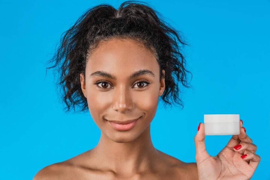 close up portrait of beautiful woman holding skin cream over blue background