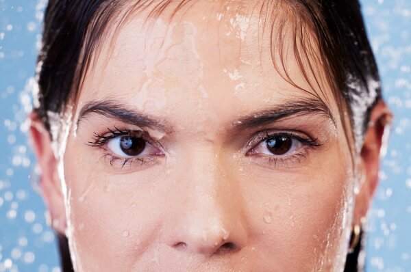 studio portrait of a young woman taking a shower against a blue background.