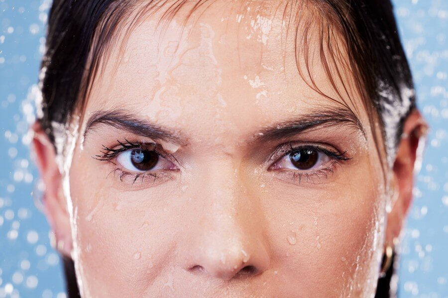 studio portrait of a young woman taking a shower against a blue background.