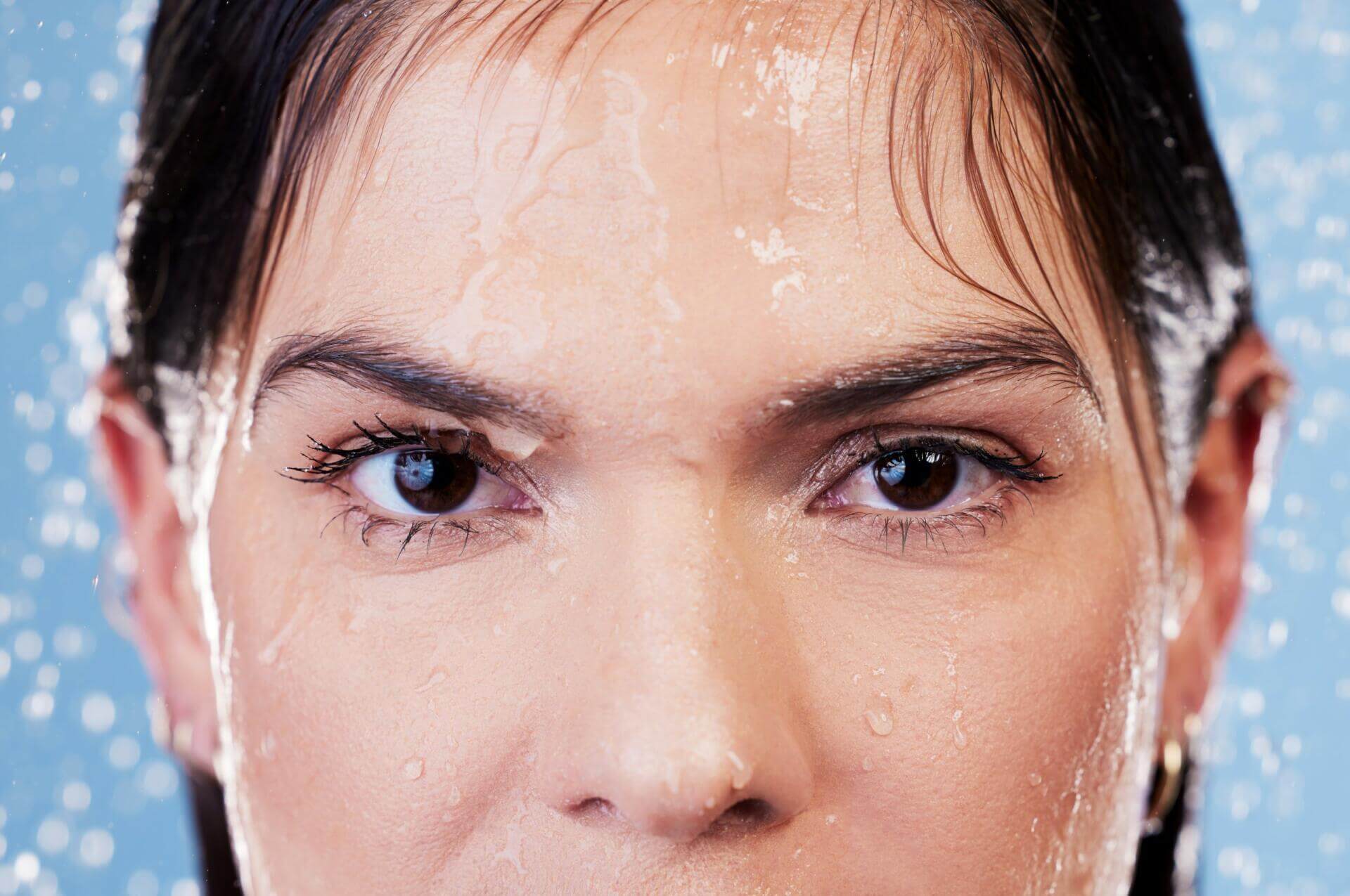 studio portrait of a young woman taking a shower against a blue background.