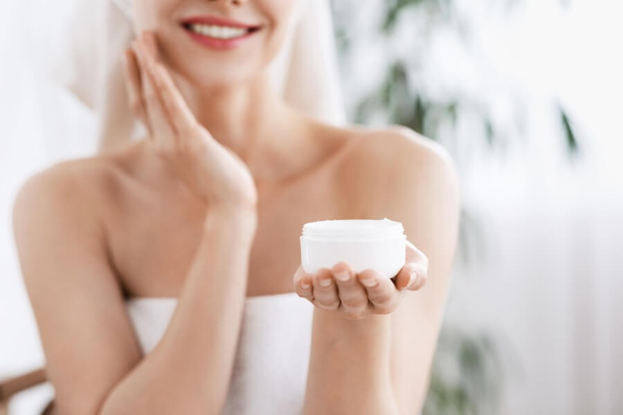 unrecognizable woman applying cream on face after shower