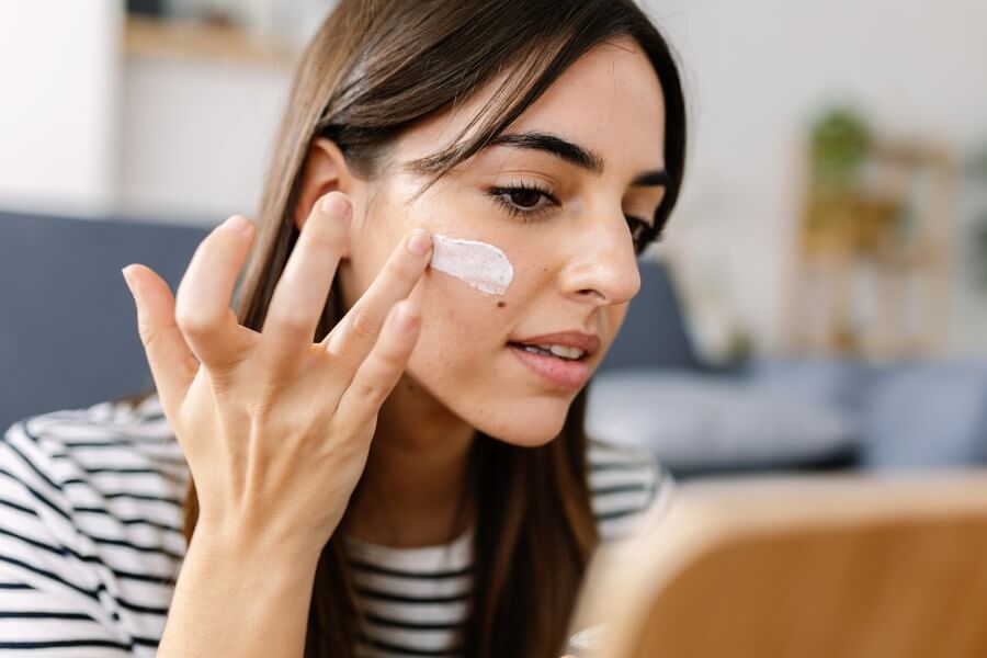 young woman using skincare product. female taking face cream to apply on facial skin