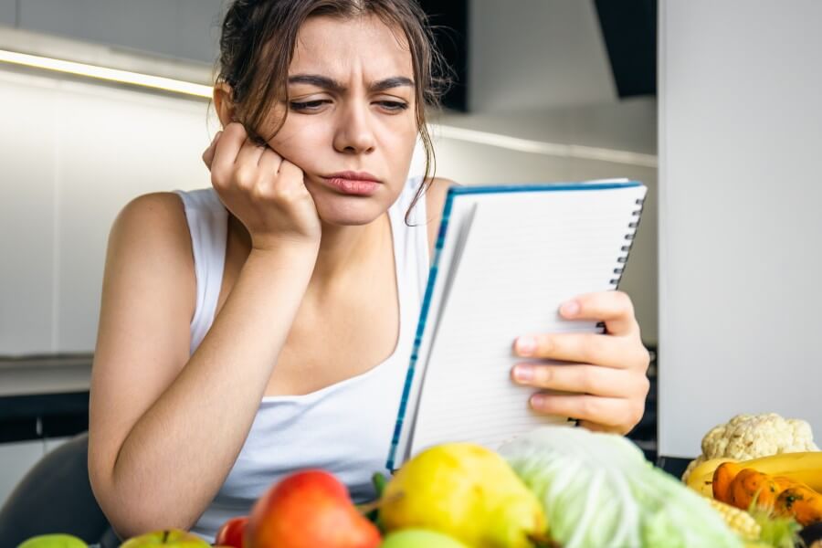 a young woman in the kitchen with a notebook among vegetables.