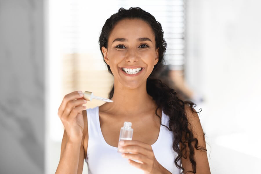 beautiful woman holding bottle with moisturizing face serum while standing in bathroom