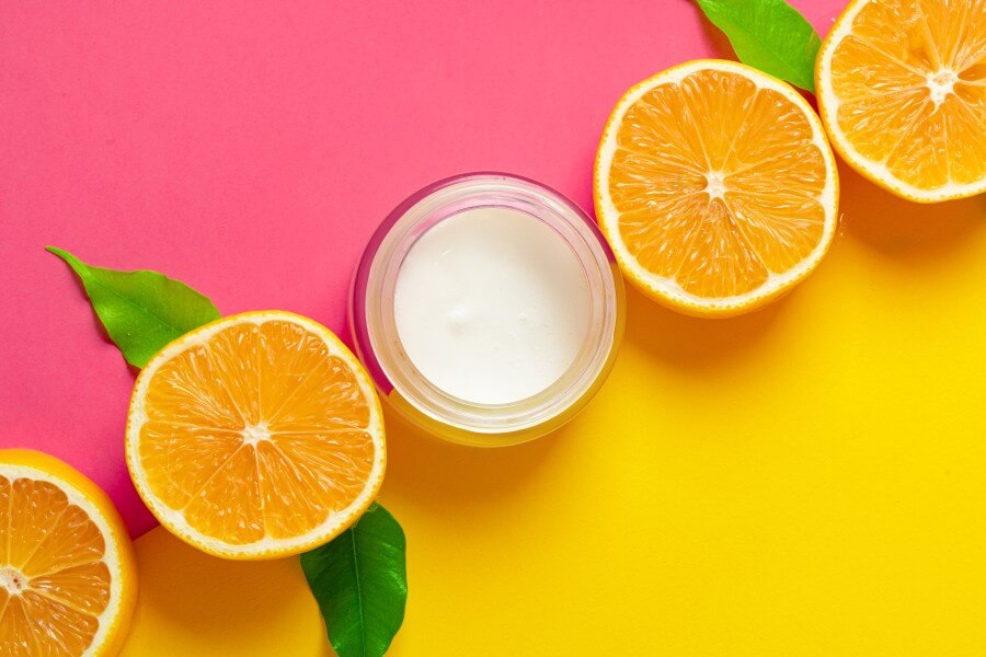 cosmetic bottle with sliced citrus fruits on bright pink background