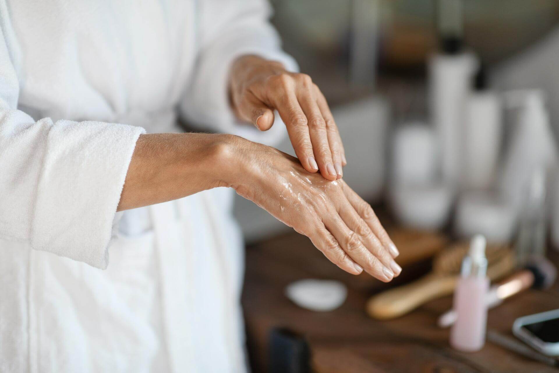 dry skin treatments. mature woman applying anti aging serum on hands at home