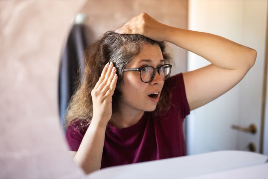 gray haired surprised caucasian middle aged woman looking at grey hair head in mirror reflection. early gray hair concept