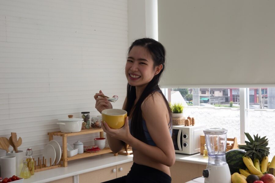 young asian woman cooking vegetable healthy food and eating or drinking in home kitchen