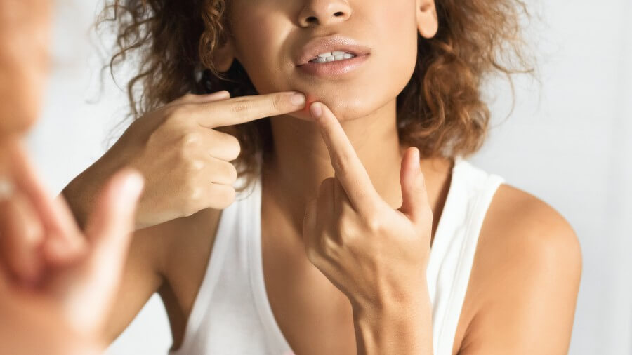 afro girl squeezing pimple looking in mirror in bathroom, panorama