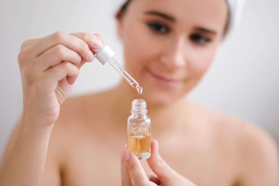 portrait of beautiful young woman with towel on head holding face oil.