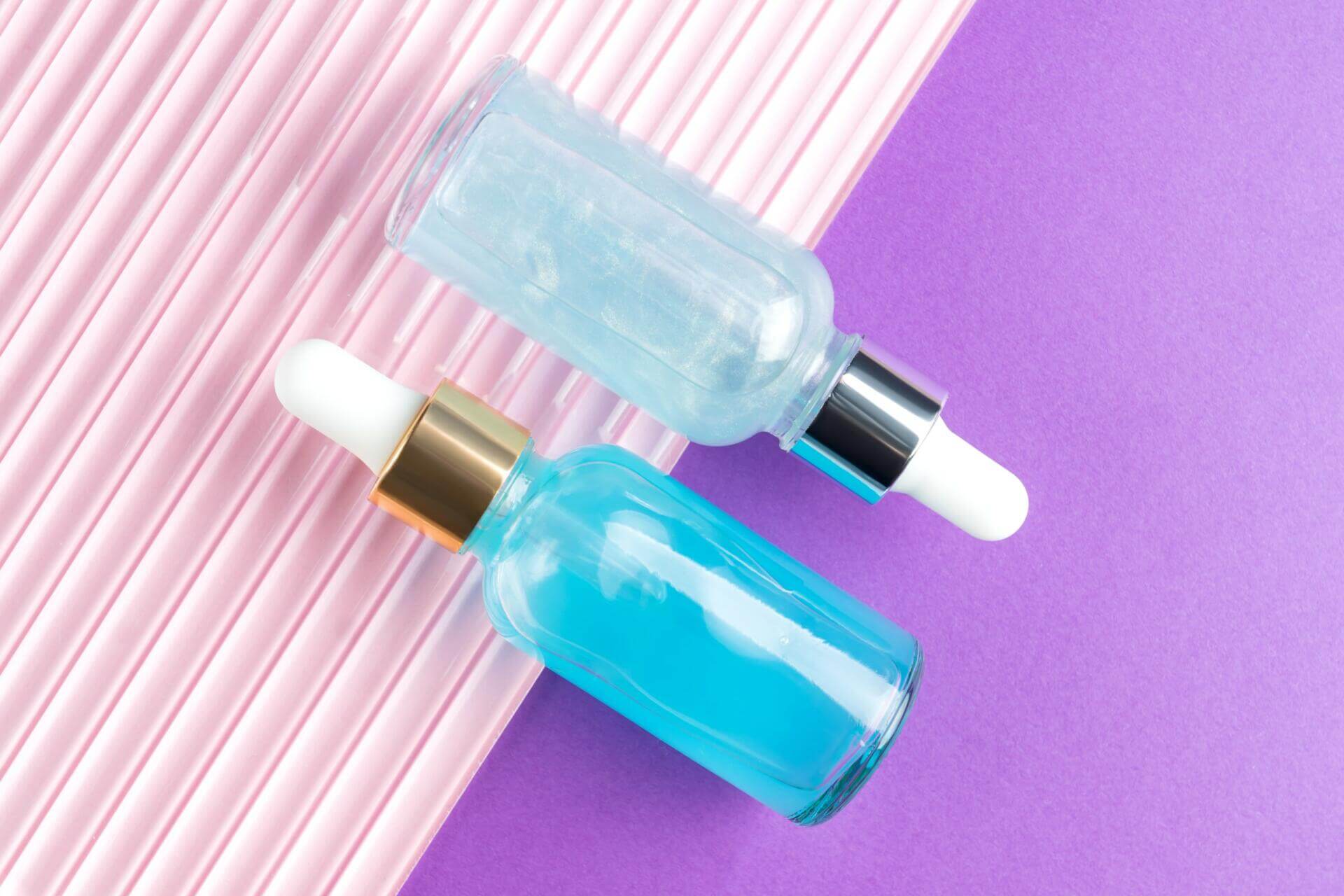 cosmetic spa medical skincare, set of glass serum bottles with collagen and hyaluron on pink and purple background. medical product adverticement for anti aging care with marine ingredients