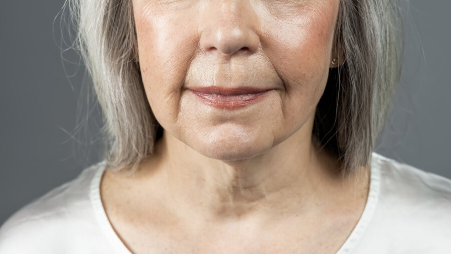 lips of smiling old european woman with gray hair, isolated on gray background, studio, cropped, close up