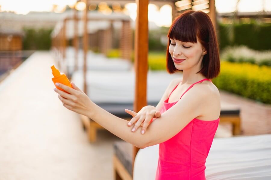 pretty woman in trendy pink swimwear applies sunscreen.