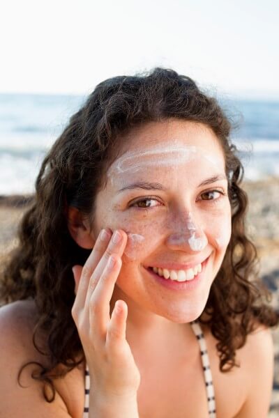 smiling woman applying sunscreen to face