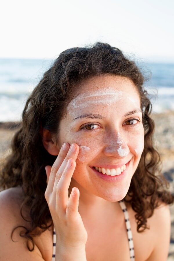 smiling woman applying sunscreen to face