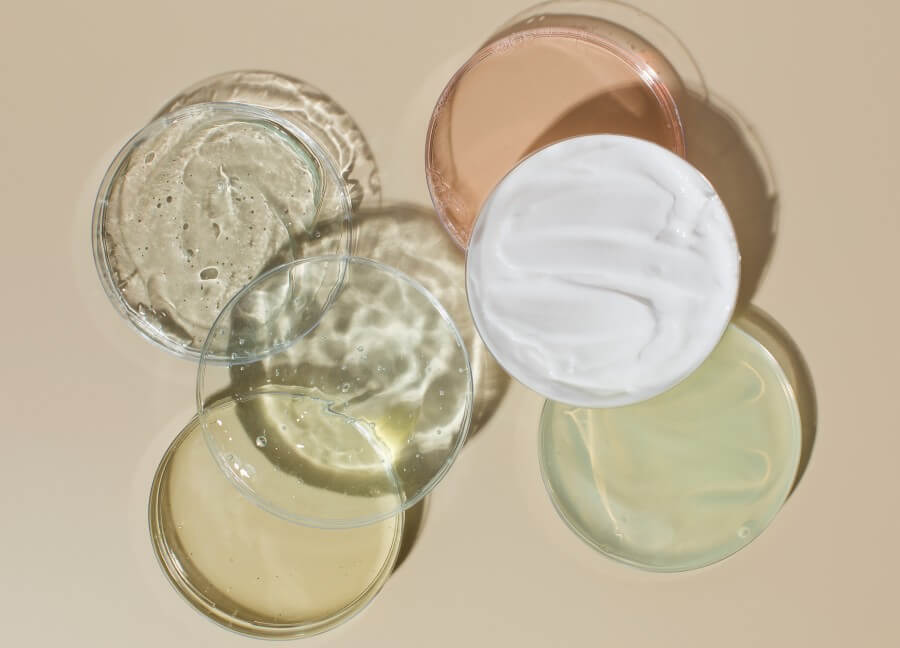 various cosmetic products in petri dishes on beige background view from above